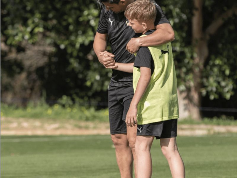 A coach encourages a young player on the pitch